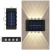 A black solar wall light with a rectangular panel and a small LED light shining onto a textured wall.