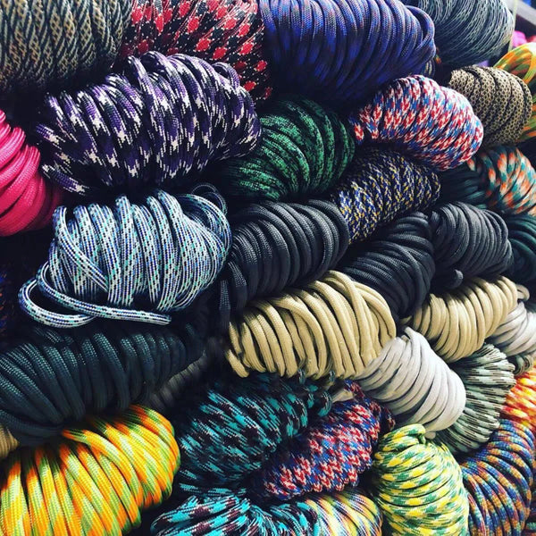 A close-up view of a large pile of various colored paracord survival ropes in different diameters.