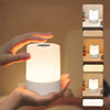 A hand is holding a white, modern LED desk lamp with a glowing light, demonstrating its use for reading or nighttime illumina