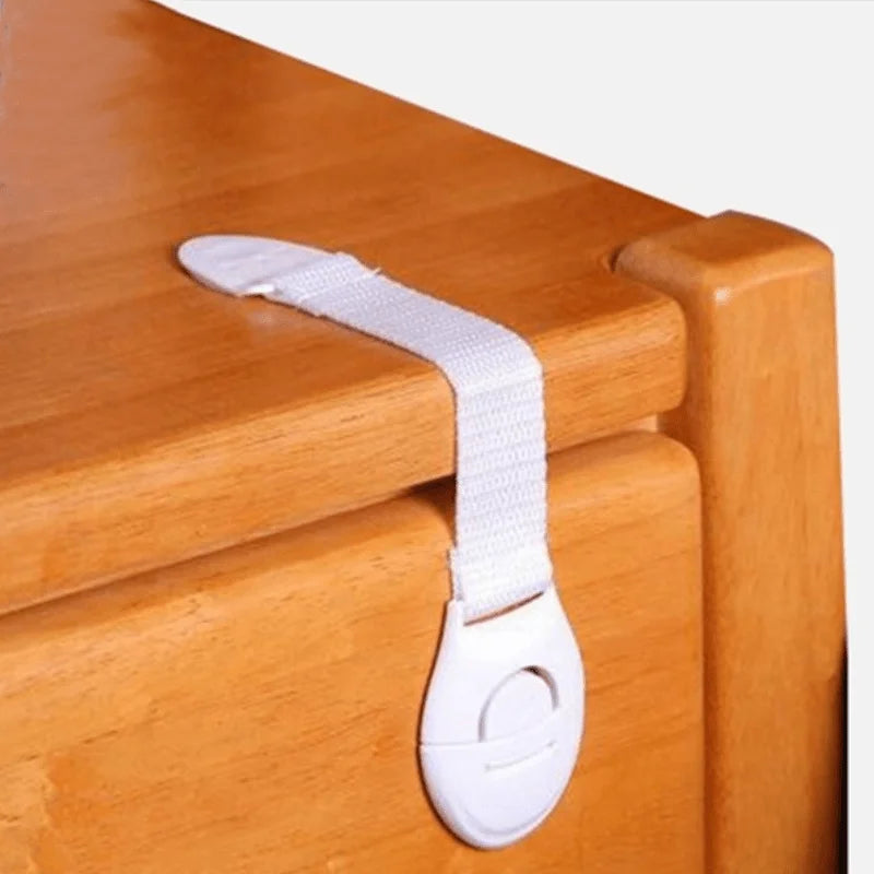 A white silicone safety clip is attached to a wooden cabinet door or drawer.