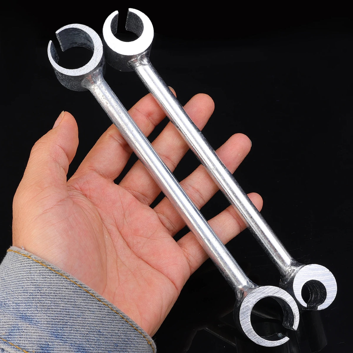 A hand holds a pair of heavy duty adjustable door hinge wrenches against a dark background.