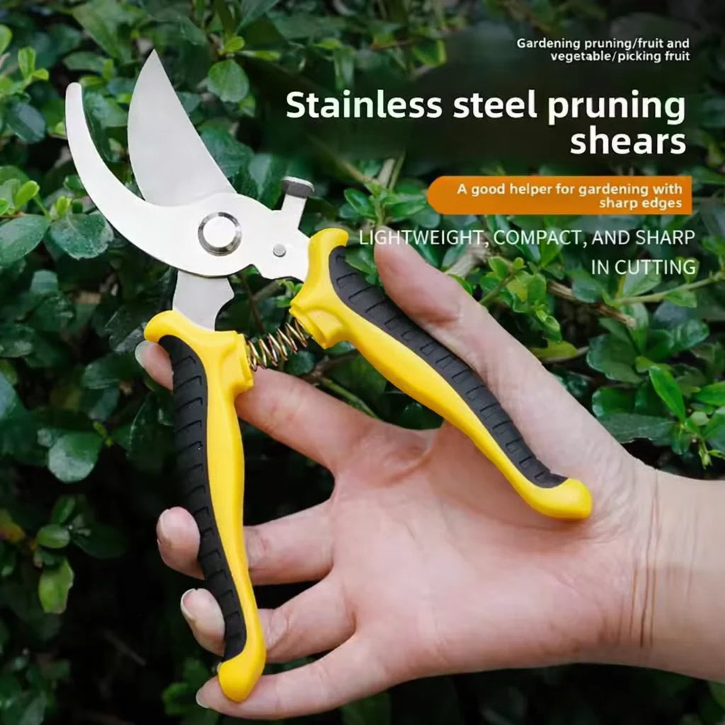 A hand holds a pair of yellow and silver stainless steel pruning shears against a green leafy background.