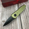 A olive green compact folding pocket knife with a black blade rests on a weathered wooden surface next to a red box.
