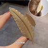 Elegant gold S-shaped metal hair clips shown being held by a hand with an inset showing the clip placement.