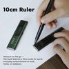 A hand holds a black 10cm ruler measuring on a white surface.