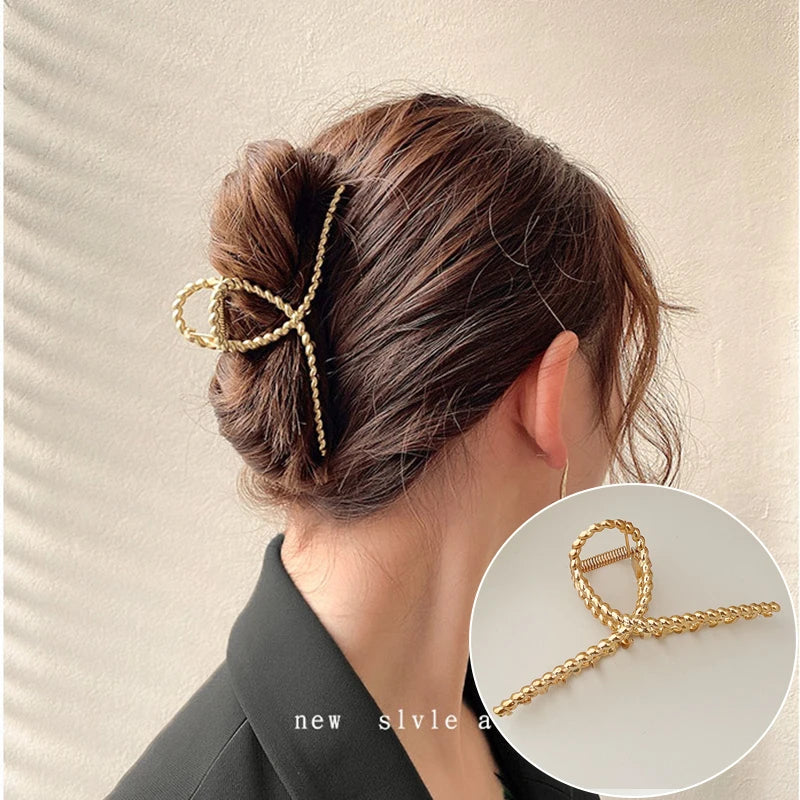 A close-up of a woman's hair styled in an elegant updo, featuring gold S-shaped metal hair clips.