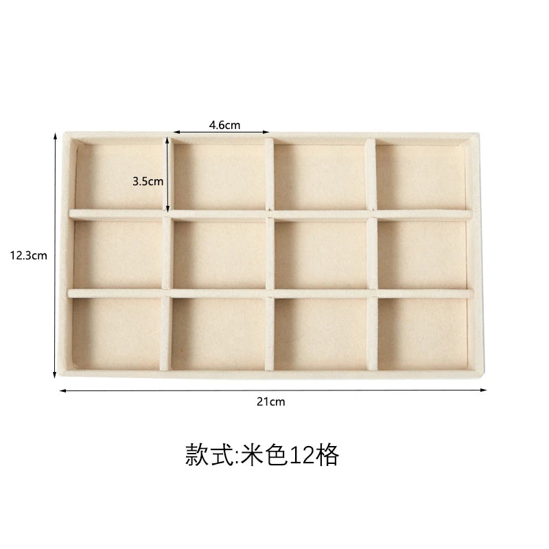A rectangular jewelry storage tray with 12 compartments made of beige plush velvet.