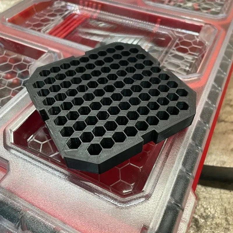 A black hexagonal drill bit organizer insert is placed inside a clear plastic tool case.