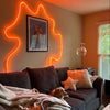 A living room wall decorated with neon orange light shaped like a flame, featuring a framed artwork and dark furniture.