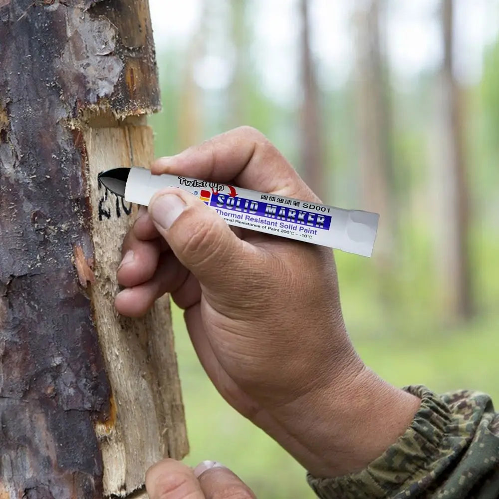 A hand holds a Twistup Solid Marker pen marking a tree trunk in an outdoor setting.