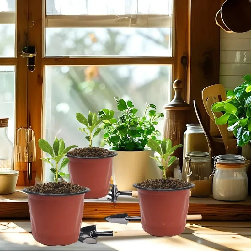 Two terracotta and pink plastic nursery pots with soil on a wooden surface near a window.