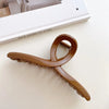 A close-up of an elegant gold S-shaped metal hair clip resting on a light surface.