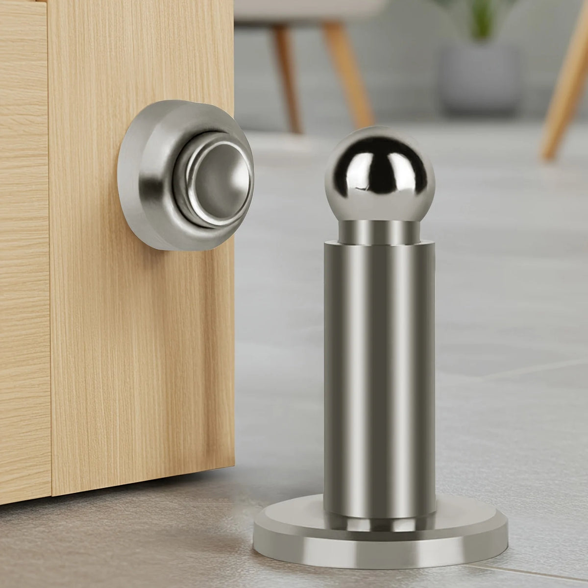 A silver magnetic door stopper with a spherical top and cylindrical body mounted on a wooden door frame.