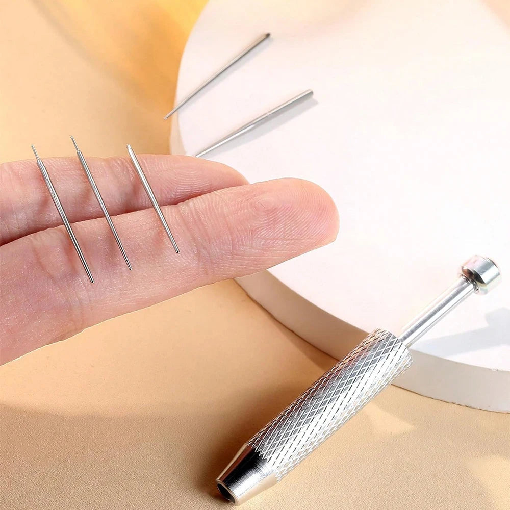 A hand holds a stainless steel piercing ball grabber kit with several long, thin needles.