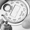 A close-up photo of a precision spark plug gap gauge set with a graduated scale and a gap opener tool.