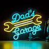 Neon-Schild mit der Aufschrift „Dad's Garage“ in hellem Blau auf dunklem Holz.