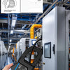 A hand holds a blue clamp meter with a digital display, measuring surge current in an industrial setting.