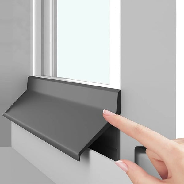 A hand is pressing a gray self-adhesive window and door water barrier strip onto a window frame.