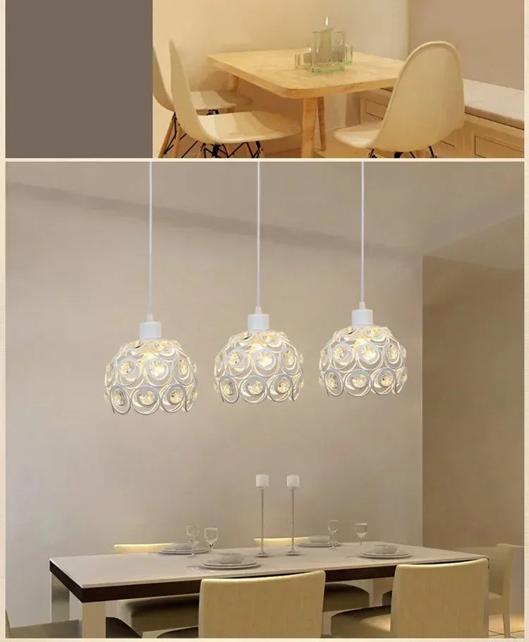 A modern crystal chandelier lamp with a white shade hangs above a wooden dining table in a bright room.