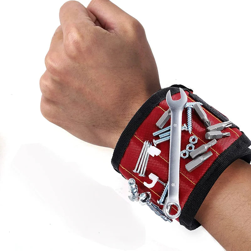 A hand is holding a red magnetic wristband filled with various tools and a screwdriver.