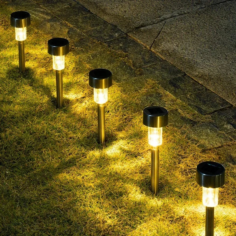 A row of solar powered outdoor garden lanterns illuminating a grassy path at dusk.
