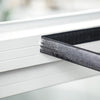 Nahaufnahme eines schwarzen selbstklebenden Moskitonetzes wird auf einen weißen Fensterrahmen aufgebracht.