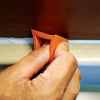 A hand is using an orange silicone seam filling tool to work on tile grout.