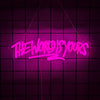 A neon sign in bright pink cursive script reads The World Is Yours against a dark grid background.