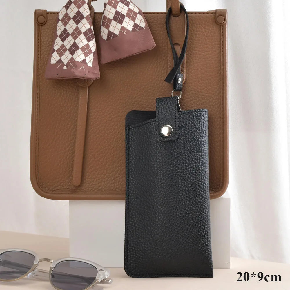A black leather eyeglasses case with a checkered fabric flap is displayed on a brown leather bag.