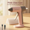 A pink glue gun is shown on a wooden surface with a stack of white glue sticks and an electrical plug nearby.