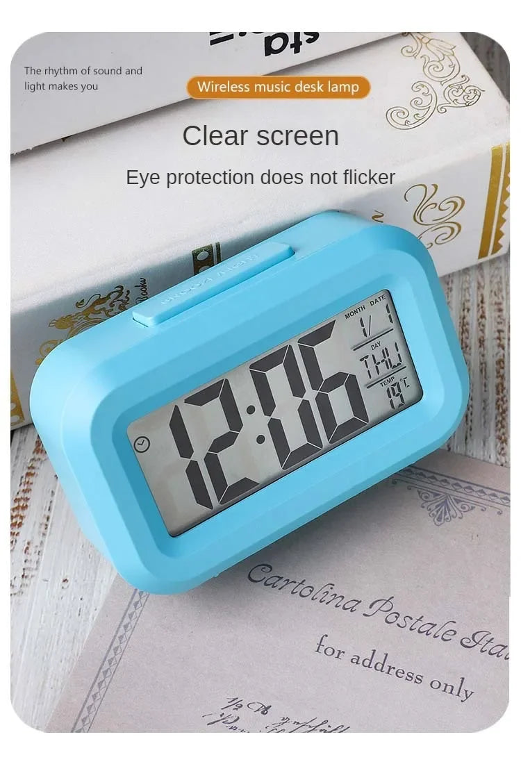 Reloj de alarma digital LED azul claro con pantalla clara, apoyado sobre una pila de papeles y un libro.