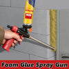 A hand is using a red foam glue spray gun to apply PU foam sealant onto a wall surface.