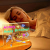 An LED acrylic message board with a night light displays a glowing birthday message on a bedside table.