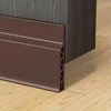 A brown door draft stopper weather stripping seal installed on a wooden floor.