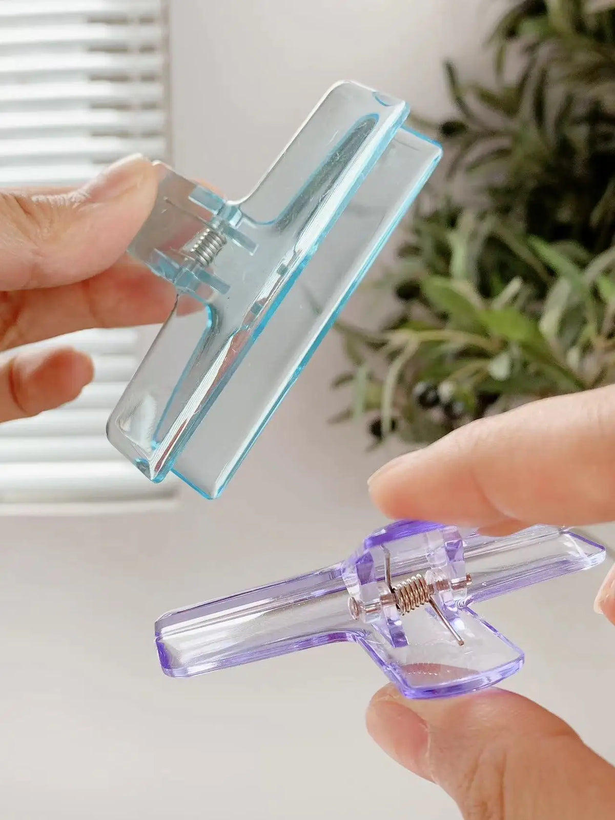 Eine Hand hält eine transparente Acryl-Federklemme und demonstriert deren Verwendung.
