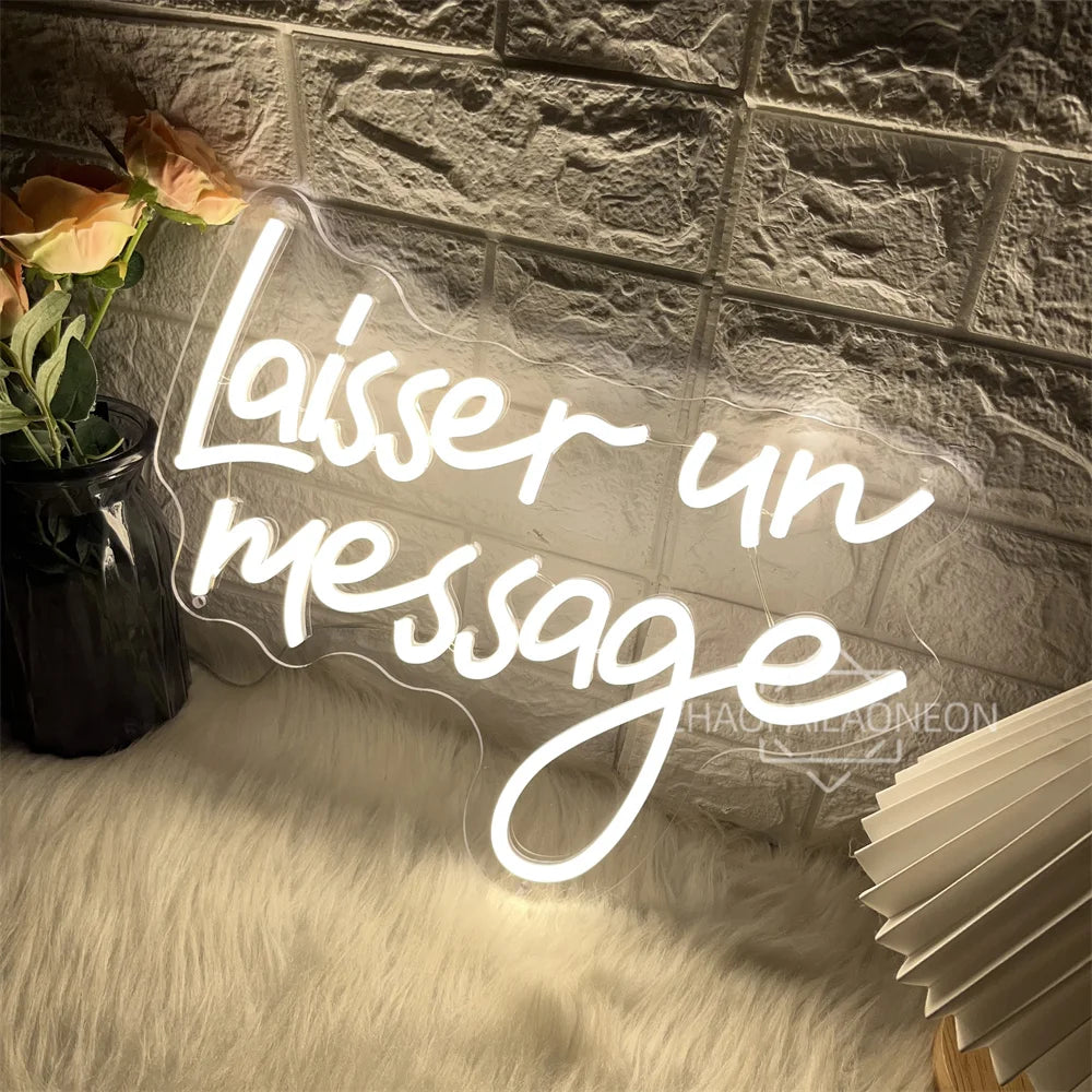 A glowing white neon sign shaped like the words 'Laisser un message' is displayed on a textured gray wall above a fluffy whit