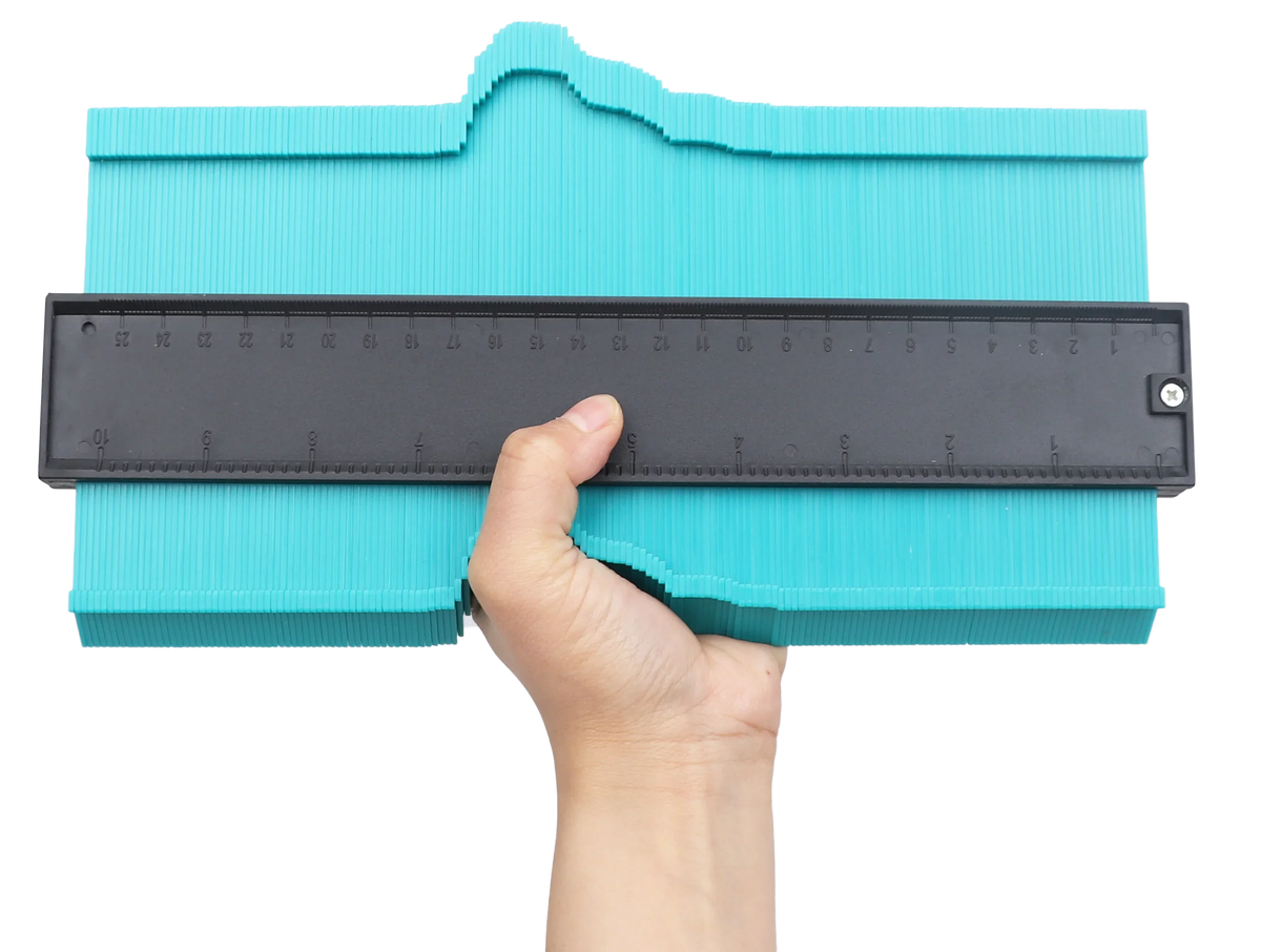 A hand is holding a black profile contour gauge against a teal-colored wooden or craft surface.