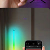 A hand holds a smartphone displaying an RGB color palette, with a floor lamp casting colorful light onto a wall.