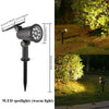 Schwarze Solar-LED-Spotleuchte auf einem Pol, die einen grünen Gartenzaun beleuchtet.
