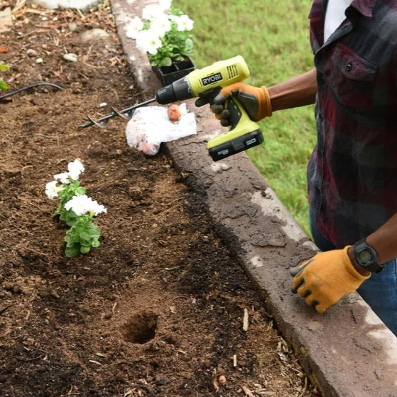 A person uses a yellow power tool to drill a hole in the soil using a heavy-duty spiral garden auger bit.