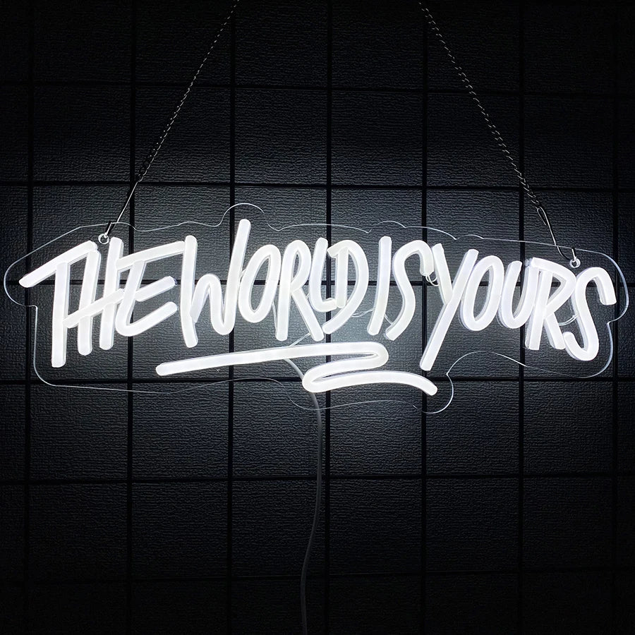 A white neon sign spelling out THE WORLD IS YOURS is suspended against a dark grid background.