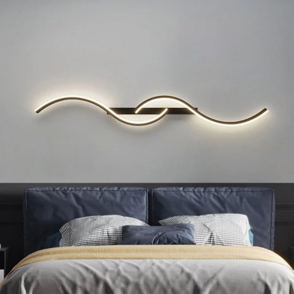 A modern LED wall sconce with a curved, illuminated light fixture mounted above a bed.