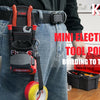 A person wearing jeans is holding a red tool pouch with a belt clip and a yellow tool on a wooden floor.