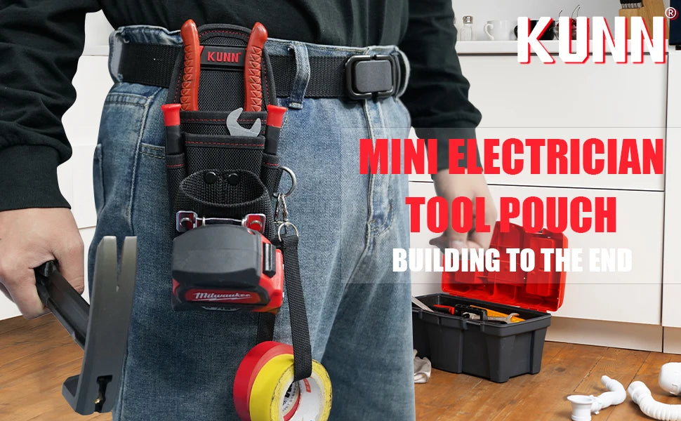 A person wearing jeans is holding a red tool pouch with a belt clip and a yellow tool on a wooden floor.