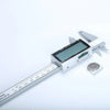 Calibrador digital vernier plateado con pantalla y escala de medición negra sobre fondo blanco.