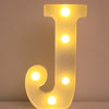 Luz nocturna de letra J amarilla brillante LED iluminando una superficie blanca.