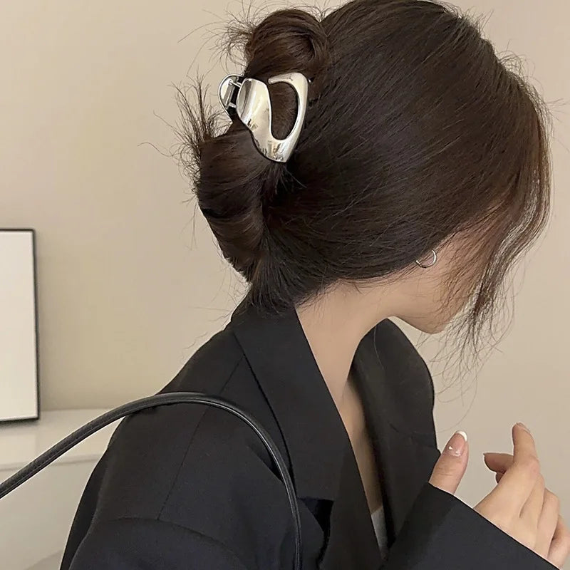 A woman is shown in profile with her dark hair styled in a bun, wearing an elegant gold S-shaped metal hair clip.