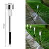 A silver solar powered outdoor garden lantern with a long metal rod and glass diffuser is shown next to a grassy path.
