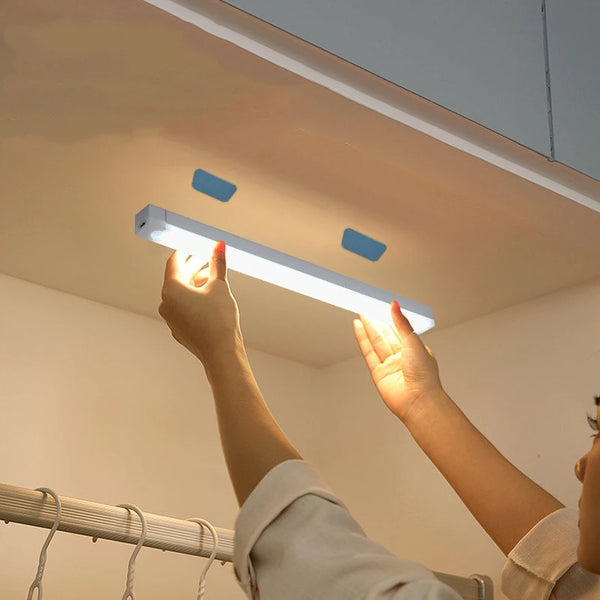 A hand is illuminating a long, white LED light bar mounted on a ceiling, demonstrating the motion sensor night light for cabi