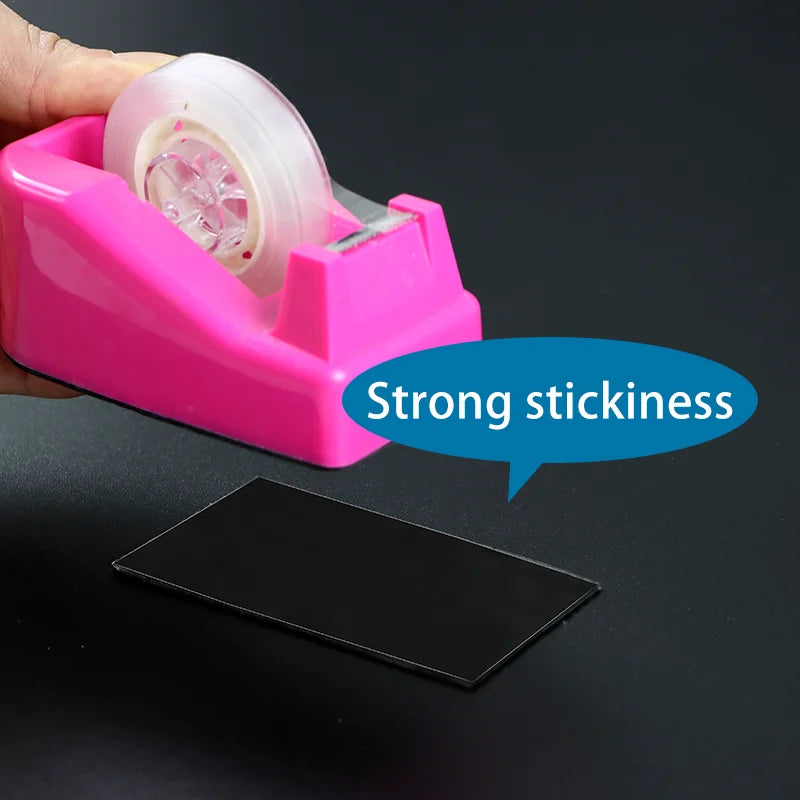 A hand is applying double-sided nano reusable adhesive tape onto a black surface.
